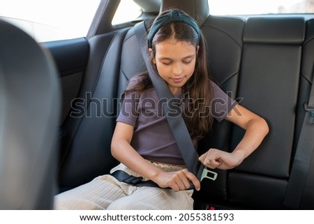 Adorable schoolgirl fastening seatbelt while sitting inside electric car Royalty-Free Stock Photo #2055381593