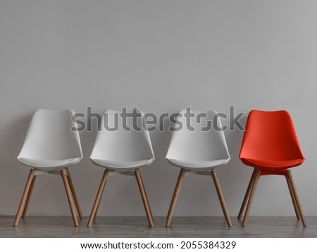 Three vacant white chairs and one red on gray wall background in office or room. Simple minimalist interior, nobody, free space. Job recruiting, leadership and business due covid-19 virus, mockup Royalty-Free Stock Photo #2055384329