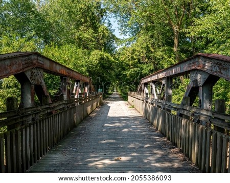 Long path leads off into the distance, surrounded by trees, the gravel multi user trail passes over a wood slat bridge, over a converted railway bridge.  No people on Katy Trail. Royalty-Free Stock Photo #2055386093
