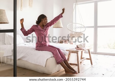 Rested African American Woman Yawning And Stretching Hands After Good Sleep Sitting On Bed In Bedroom, Wearing Pajamas. Happy Well-Slept Female Waking Up Enjoying Weekend Morning At Home Royalty-Free Stock Photo #2055392744