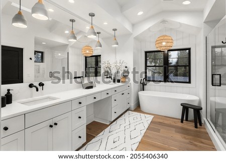 Beautiful ensuite bathroom in new farmhouse style luxury home with double vanity, freestanding soaker bathtub, mirror, sinks, shower, and hardwood floor. Royalty-Free Stock Photo #2055406340
