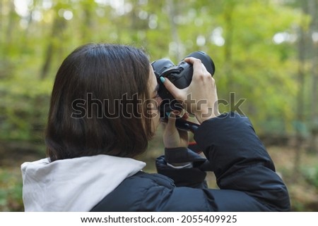 young woman taking photo with dslr camera in forest, close up portrait