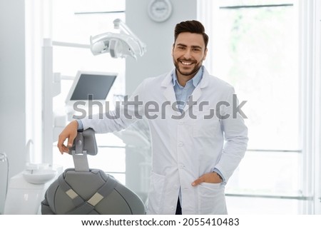 Handsome caucasian young man doctor posing at newest dental clinic, copy space. Happy bearded male dentist greeting patients or inviting to visit brand new modern dental clinic, healthcare concept Royalty-Free Stock Photo #2055410483
