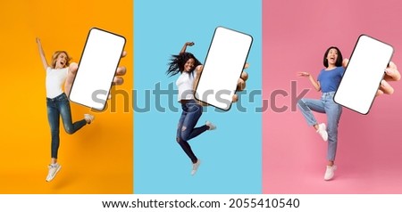 Happy glad excited international ladies jumping, fun, dancing and show phone with blank screen, isolated on colored background, panorama, collage. Positive emotions, great offer, new app and website Royalty-Free Stock Photo #2055410540