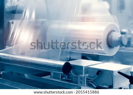 The operation of automatic plastic bag production machine with lighting effect. Close-up of the roller of the plastic bag production machine in the light blue scene. Royalty-Free Stock Photo #2055415886
