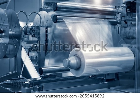 The operation of automatic plastic bag production machine with lighting effect. Close-up of the roller of the plastic bag production machine in the light blue scene.