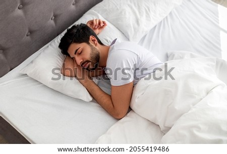 Asleep young arab man sleeping, resting peacefully in comfortable bed, lying with closed eyes, free space. Recreation, deep male sleep, time to rest and nap concept Royalty-Free Stock Photo #2055419486