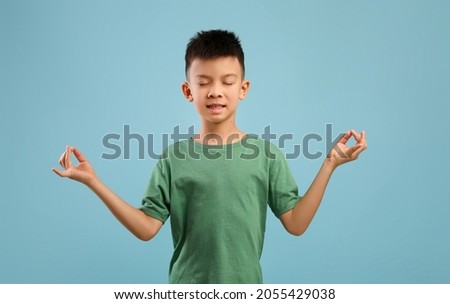 Zen. Relaxed Little Asian Boy Meditating With Closed Eyes Over Blue Background, Calm Korean Male Child Practicing Yoga, Keeping Hands In Mudra Gesture While Posing In Studio, Copy Space