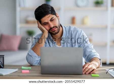 Overworked arab man sitting at workplace and napping while working on laptop computer, placed head on hand, feeling tired, copy space. Freelance stress concept