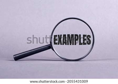 Magnifying glass with EXAMPLES lettering on a gray background. Royalty-Free Stock Photo #2055431009