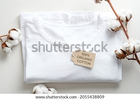 Organic cotton t-shirt with cotton flowers on white background. Flat lay, top view. Eco clothing, sustainable lifestyle, fashion concept. Royalty-Free Stock Photo #2055438809