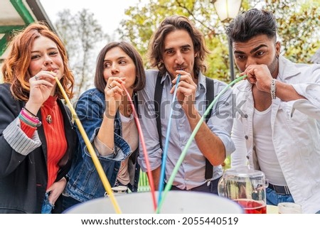 group of multi-cultural friends having fun at the garden party sucking beer from colorful straws from a cooler
