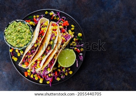 Vegetarian tacos with sweet corn, purple cabbage and tomatoes on a black plate. Tacos with vegetables and guacamole sauce on dark background. Copy space. Top view