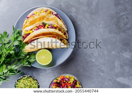 Mexican tacos with vegetables and guacamole on gray background. Vegan tacos with corn, purple cabbage and tomatoes on a gray plate. Copy space. Top view