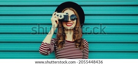 Portrait of happy smiling young woman photographer with vintage film camera on colorful blue background