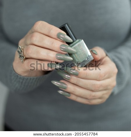 Female hand with long nails and gray green manicure with bottles of nail polish