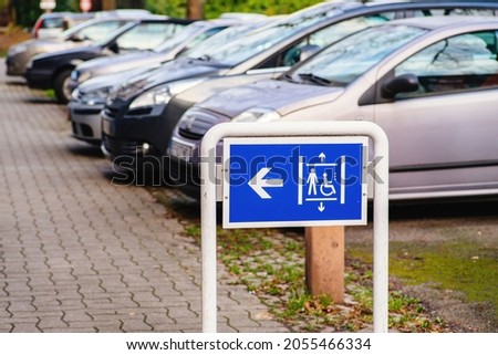 Elevator sign for people ion wheelchair with large row of defocused cars parked in background