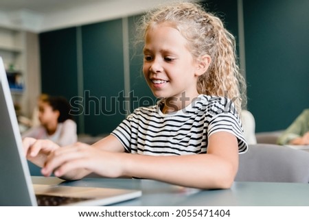 Small girl schoolgirl kid pupil student using laptop at school classroom for doing homework, projects, writing test online, listening to e-lessons e-classes remotely