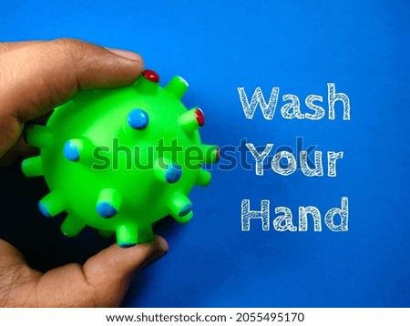 Text Wash Your Hand with hand holding rubber toy coronavirus on blue background.