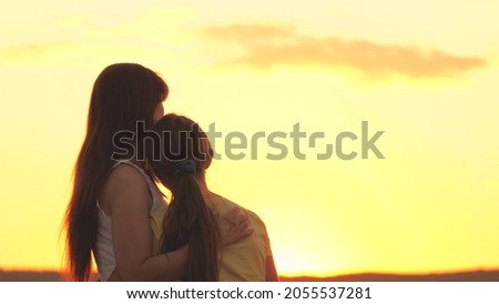 mother hugs teenager girl at sunset in sky, difficult age, kid in arms of her beloved mother in sun, child daughter with her parent meets dawn on trip, concept of happy family, parental help support Royalty-Free Stock Photo #2055537281