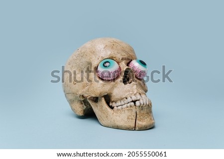 Scull with crooked toy eyes facing outside. Halloween theme. Over blue background. Royalty-Free Stock Photo #2055550061