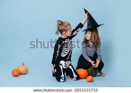 Boy in skeleton costume taking a witch hat off of a girl, she looks at him. They are dressed for halloween. Over blue background.