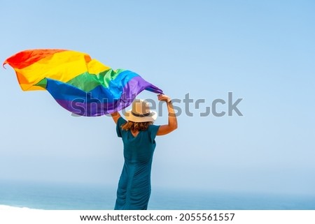 Lgbt symbol, an unrecognizable lesbian person from behind waving the flag and the blue sky in the background