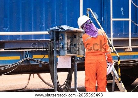Action of a safety officer in orange coverall and white hardhat is looking on electricity junction box for safety inspection. Industrial working people photo scene.