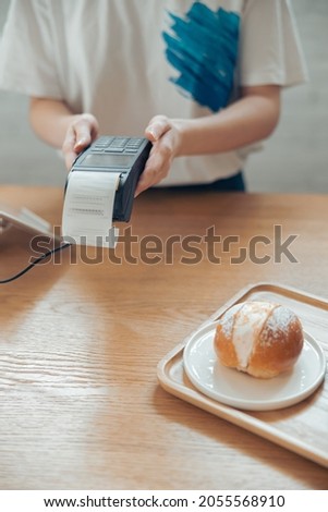 Female barista using terminal for contactless payment in coffee shop