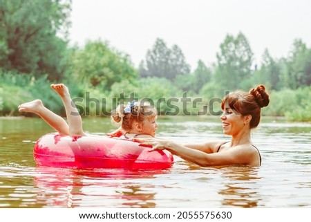 mom with a little daughter swimming in the river, daughter sitting on her mother's back