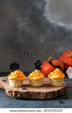 Festive Halloween cupcakes decorated with black toppings. Dark background with pumpkin and copy space for text, selective focus. Bakery menu