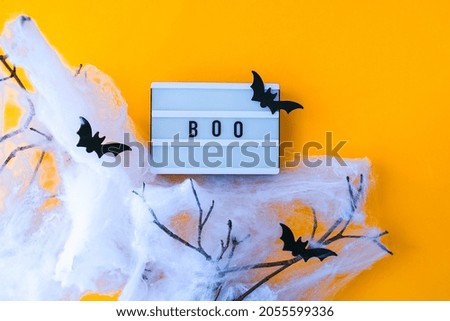 Lightbox with word BOO and halloween party decorations. Bats on dry tree branch with spider net for Halloween on orange background. Top view flatlay