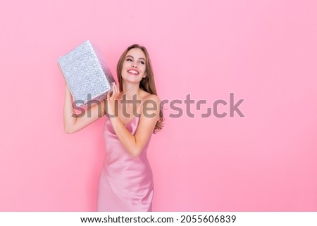 Image of happy beautiful girl shaking box with gift wonder what inside wrapped box stands on pink background. Celebration concept. Happy birthday. New Year. 8 March 