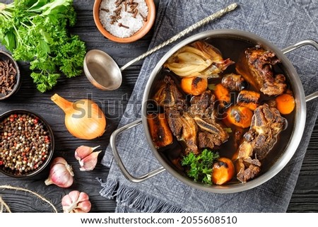 beef broth of beef meat on bones slow cooked with charred vegetables: carrot, onion, garlic, and spices served in a pot on a wooden table, top view, flat lay, close-up, macro