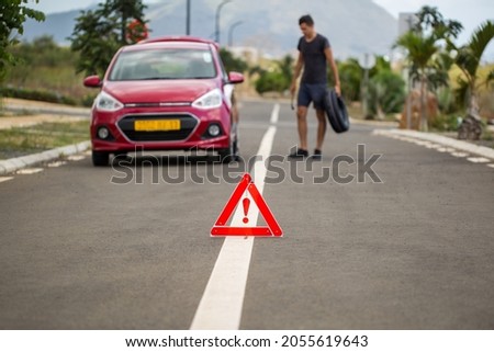 man holds the spare tire against a broken-down car on the background of mountains and palm trees
