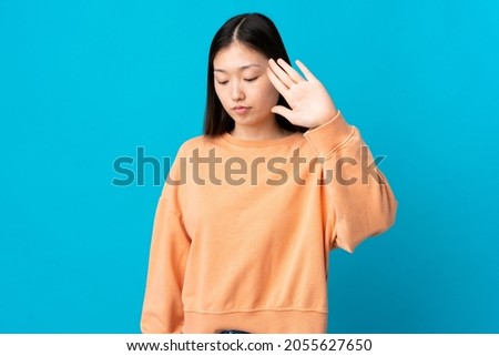 Young Chinese girl over isolated blue background making stop gesture and disappointed