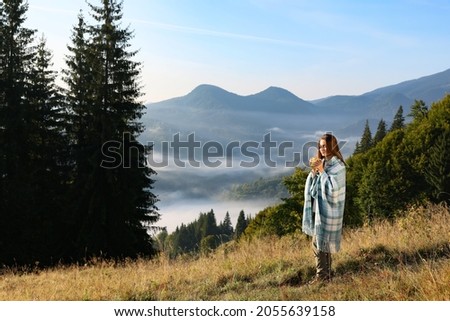 Woman with cozy plaid enjoying cup of hot beverage in mountains Royalty-Free Stock Photo #2055639158