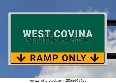 West Covina logo. West Covina lettering on a road sign. Signpost at entrance to West Covina, USA. Green pointer in American style. Road sign in the United States of America. Sky in background