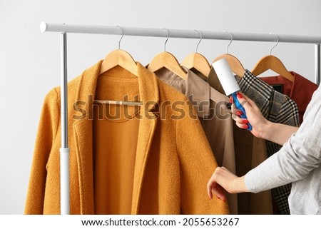 Woman cleaning coat with lint roller on light background Royalty-Free Stock Photo #2055653267