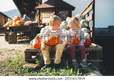 Family and kids at fall season. Preschool children sitting in pile of pumpkins at local farm market. Children picking pumpkin on Halloween or Thanksgiving holiday. Boy and girl outdoor at countryside.