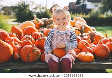 Autumn harvest of pumpkins. Child picking orange pumpkin at farm market or seasonal festival. Cute little girl playing among pumpkins. Thanksgiving holiday season and Halloween.