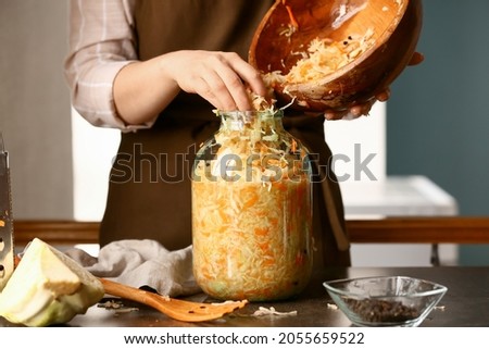 Woman putting tasty sauerkraut into glass jar on table in kitchen, closeup Royalty-Free Stock Photo #2055659522