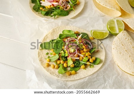 Parchment with tasty vegetarian tacos on light wooden background