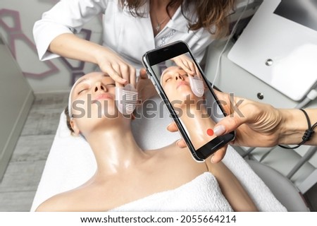 Hand holding smartphone making online live video stream of cosmetician doctor facial care procedure tutorial for online workshop master class in social media network. Remote distance learning concept
