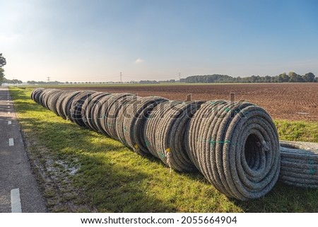 Rolls of new permeable pipes ready for the construction of a subsurface drainage system in a plot of farmland of a Dutch polder. The photo was taken on a sunny day in the autumn season. Royalty-Free Stock Photo #2055664904