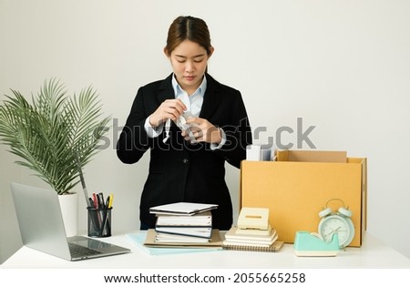 A woman office worker is unhappy with being fired from a company packing things into cardboard boxes. The Young woman was stressed and disappointed by being fired. concept of layoffs and unemployment.