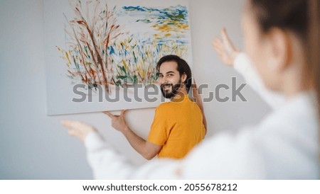 Young couple arranging new flat, hanging up painting, new home and relocation concept. Royalty-Free Stock Photo #2055678212