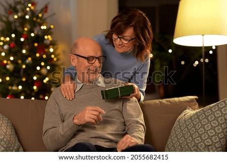 winter holidays and people concept - happy senior couple with gift box at home over christmas tree lights on background
