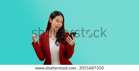 Excited happy woman looking at the phone screen, celebrating an online win, overjoyed young female screaming with joy, isolated over a blue color background