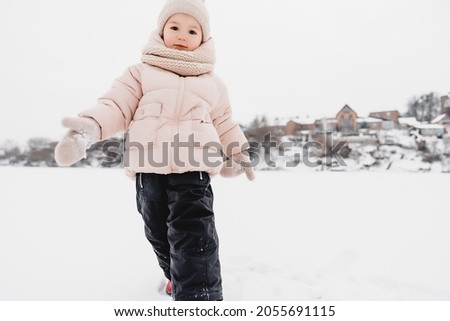 Winter cheerful little child playing throws up snow outdoors. The girl is lying in the snow, playing and having fun.